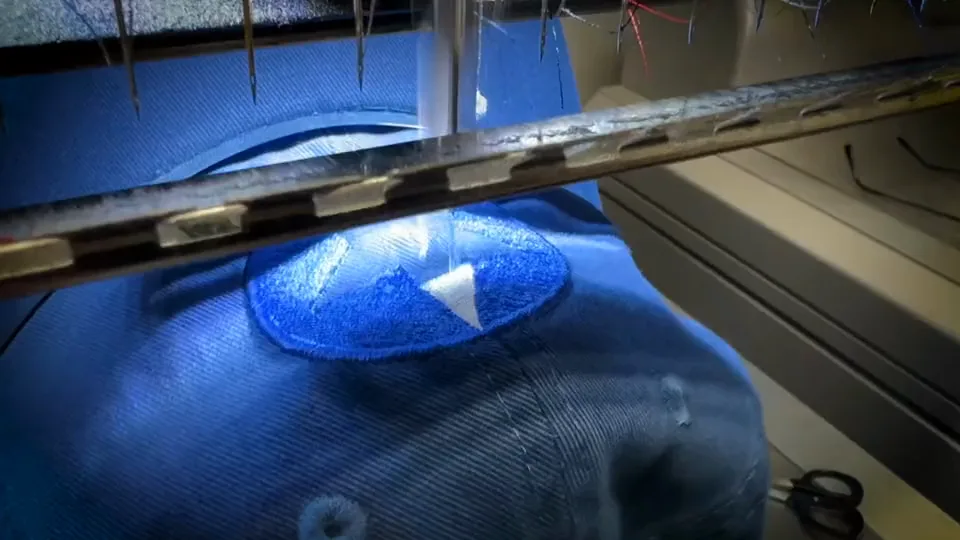 Embroidery machine stitching a blue and white logo onto a blue cap