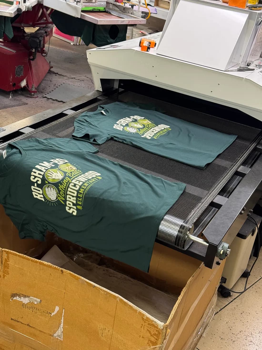 Forest green Bella+Canvas 3001 spirit tees for Sprucewood Elementary coming off the curing dryer belt