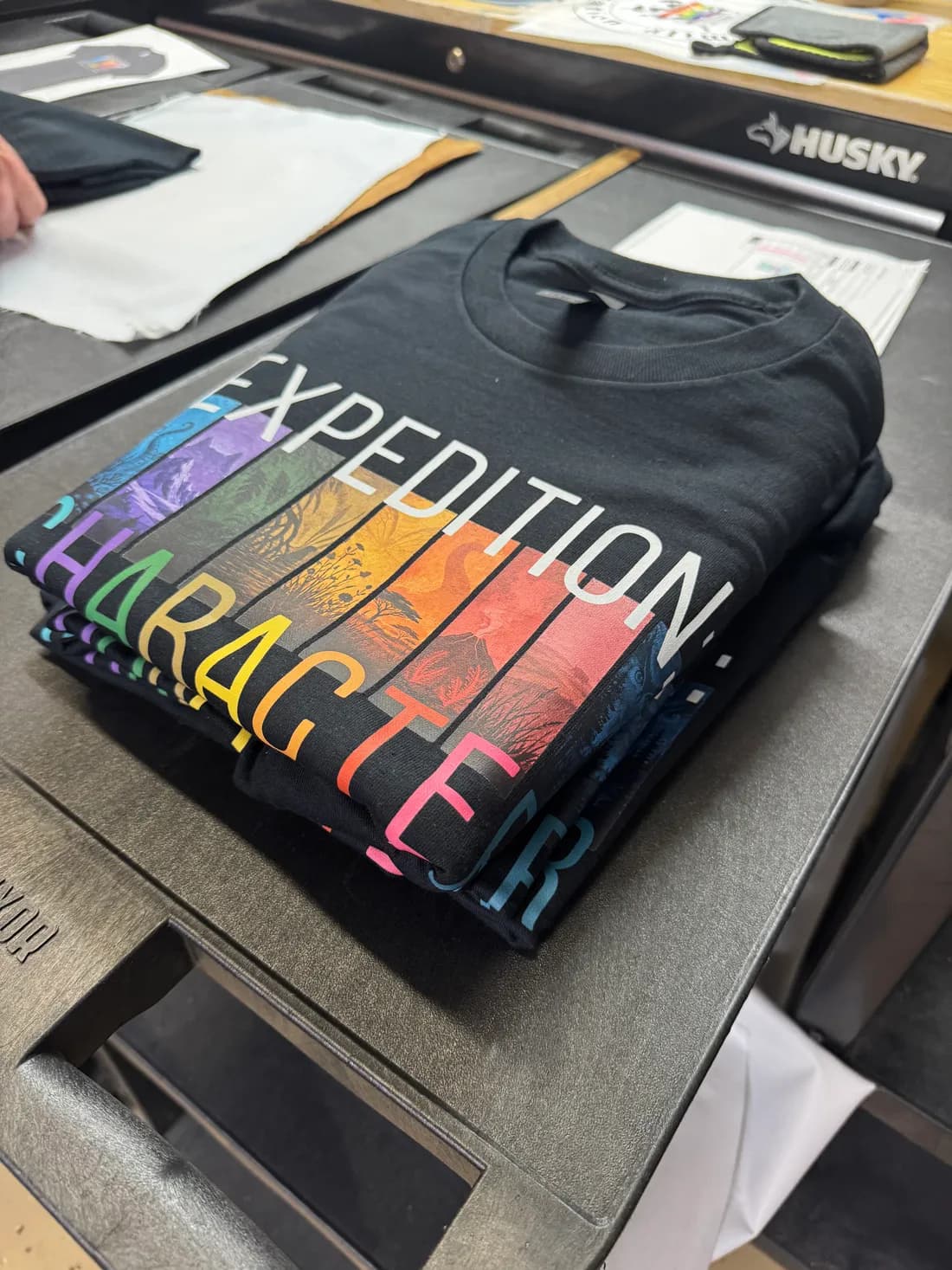 Stack of black Gildan 5000 tees with a full-color Expedition Character DTF print on the front