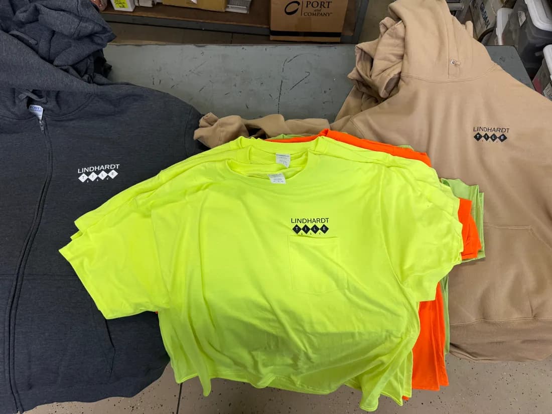 Hi-vis pocket tees, charcoal zip fleece, and tan hoodies all printed with the Lindhardt Tile logo