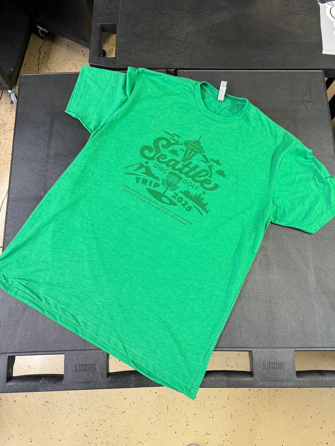 Heather green Next Level 6210 tee with a tone-on-tone Seattle Disc Golf Trip 2025 print listing the courses played