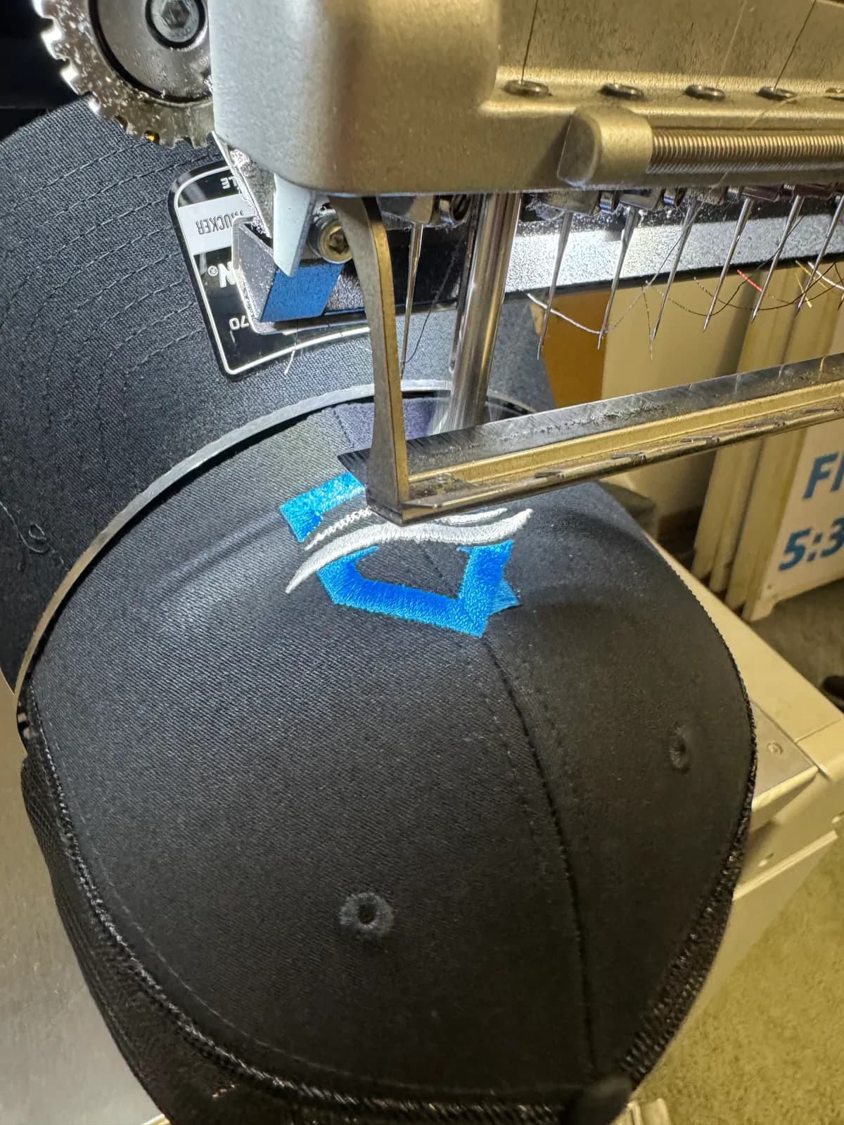 Navy cap on the embroidery machine with a blue and white logo being stitched