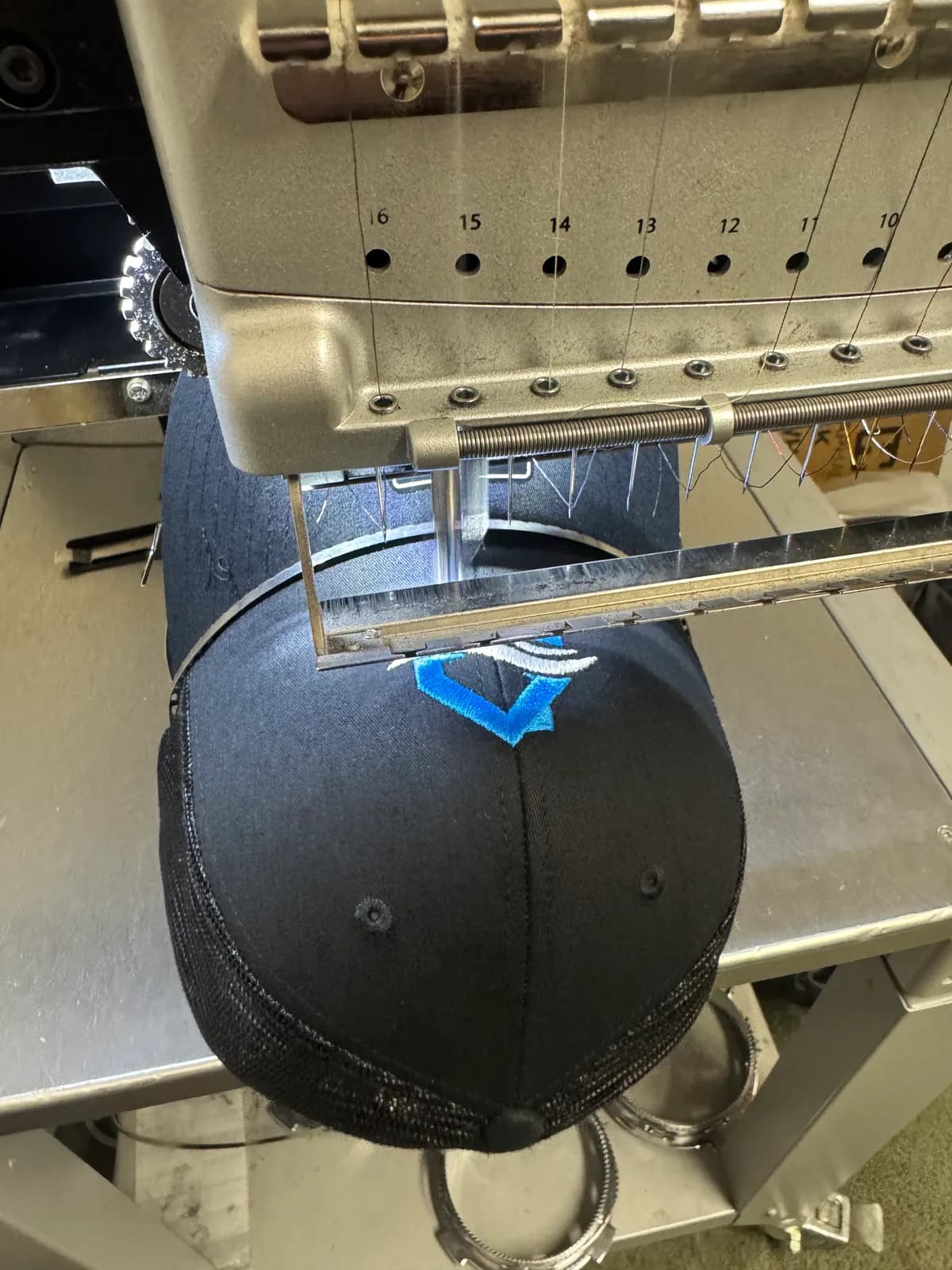 Navy cap on the embroidery machine with a South Salt Lake air duct company's blue logo freshly stitched