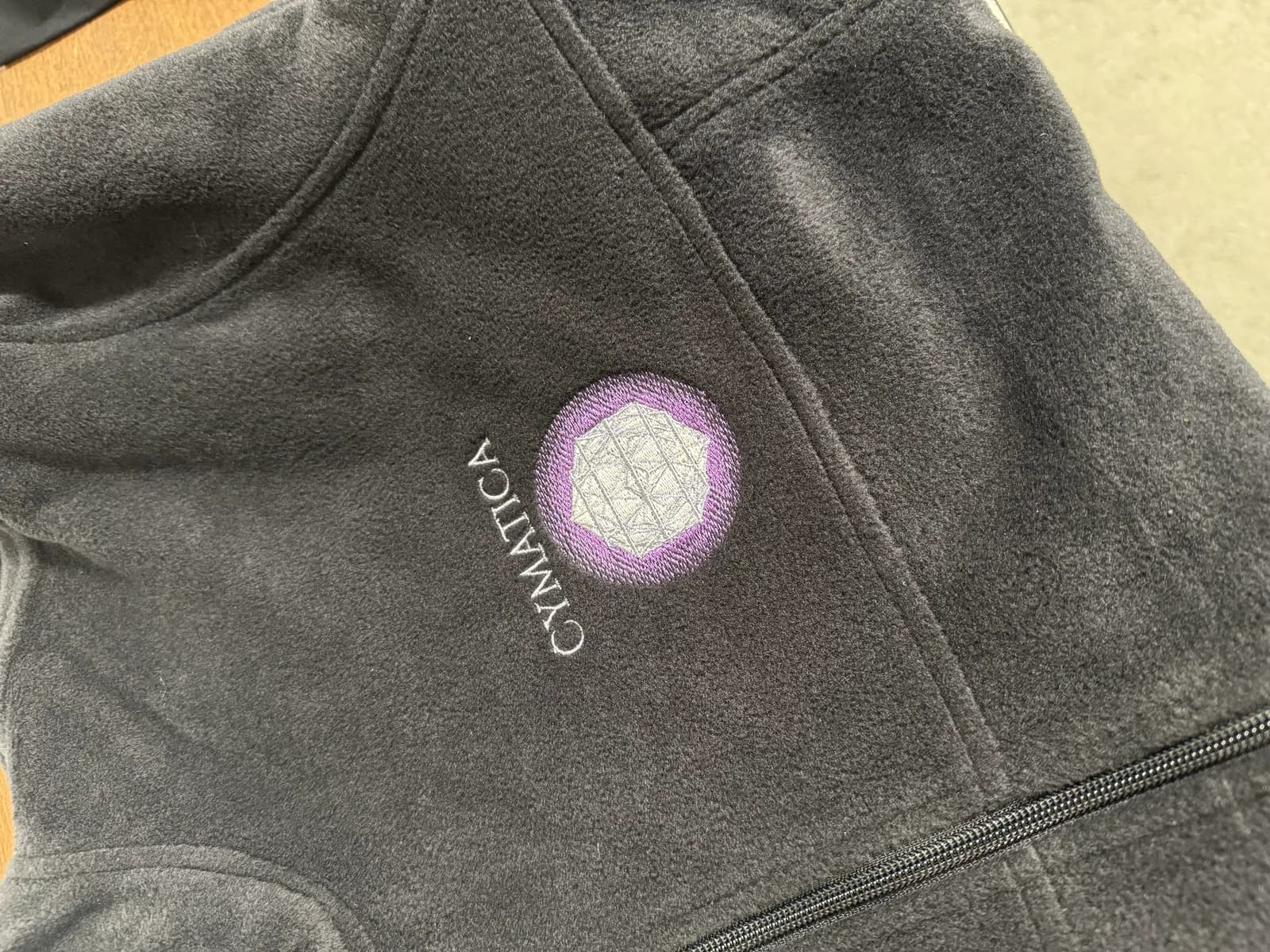 Embroidered geometric sound-healing logo with a purple ring on a charcoal fleece jacket